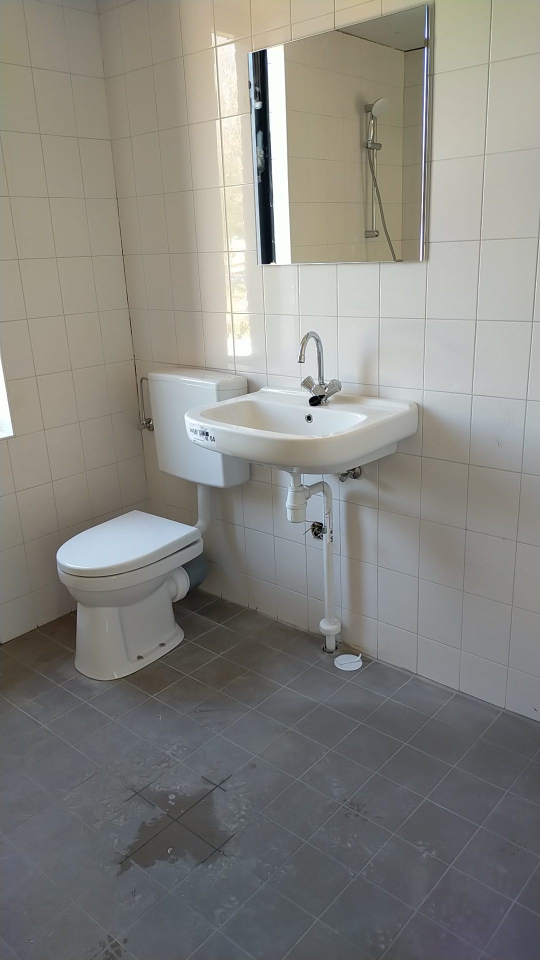 Een afgewerkte toiletruimte met hangende wastafel, spiegel en toilet op een grijze tegelvloer
