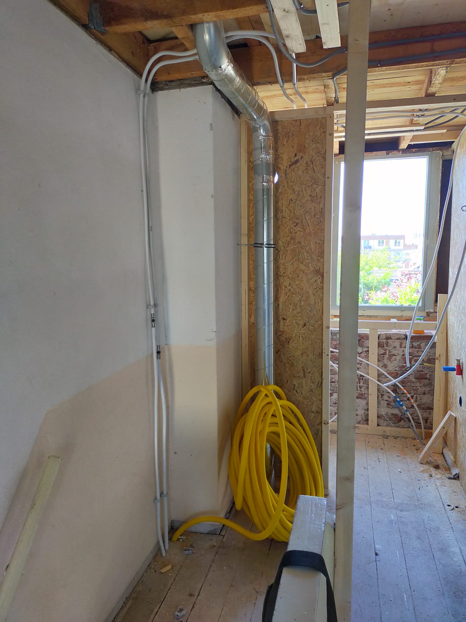 Een woning in renovatie met nieuw leidingwerk langs wand en plafond, een ventilatiekanaal en een gele slang